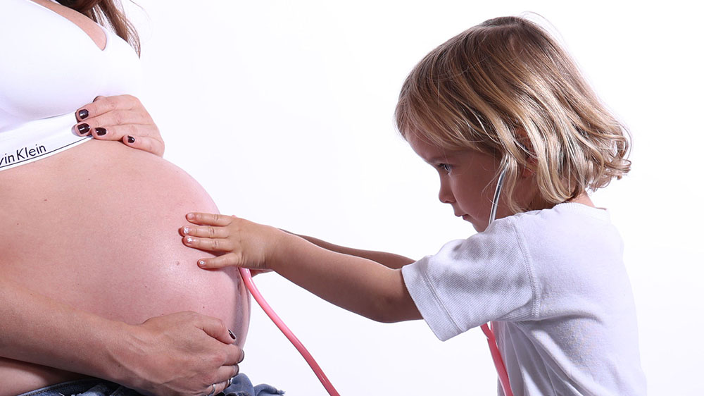 Babybauchshooting mit Geschwisterkind - große Schwester küsst den Babybauch
